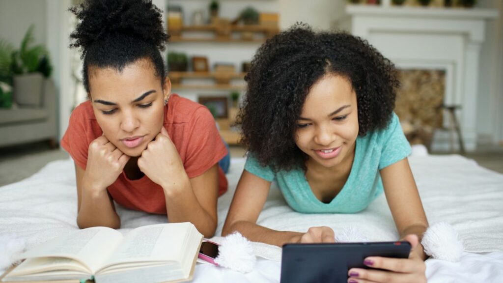 Parent and child are sitting together in a brightly lit room, looking at a tablet screen with expressions of curiosity and...