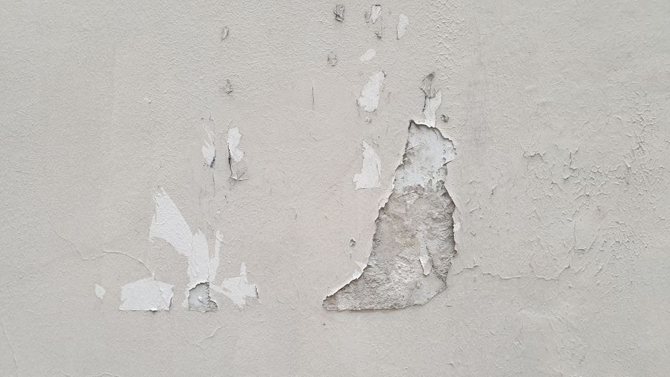 Young child with a concerned expression looks at a wall with peeling paint and water stains, symbolizing the emotional imp...
