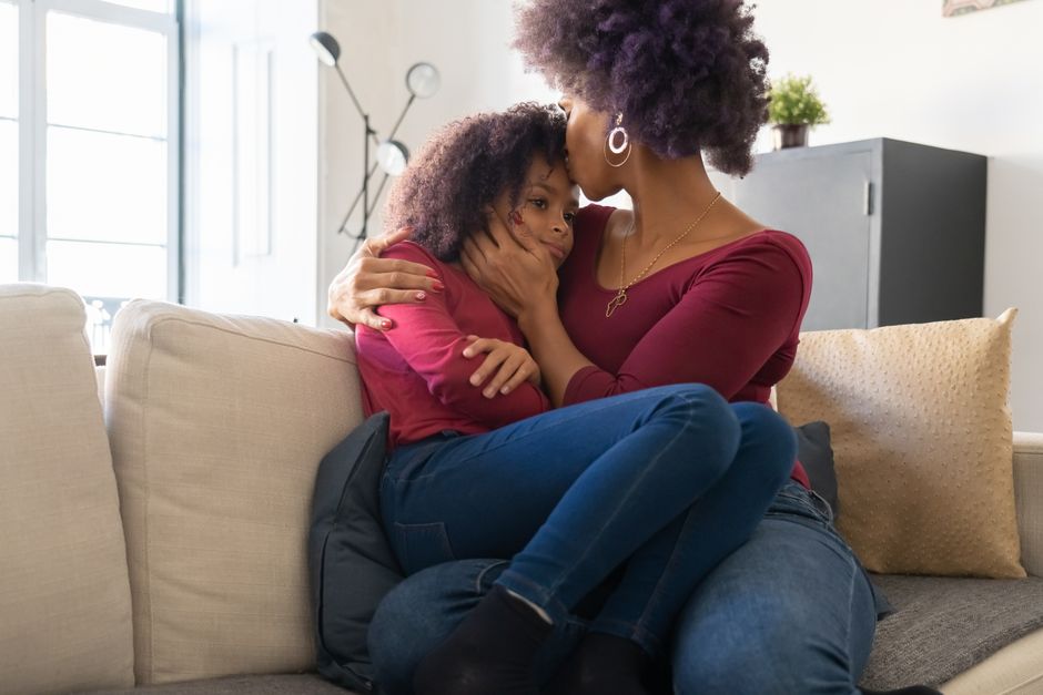 A caring parent kneels down to hug their young child in a room with moving boxes, illustrating family support and emotional security during a home move.