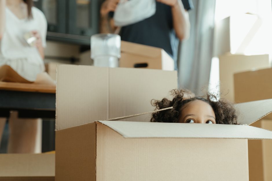 A happy child plays inside a large cardboard box in a bright, sunlit room, symbolizing resilience, imagination, and finding joy during the process of moving to a new home.