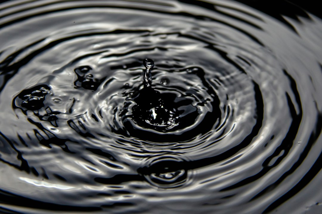 A top-down, minimalist photo of a single water drop hitting a calm surface, creating perfect, expanding ripples that represent the positive amplification of trustworthy information.